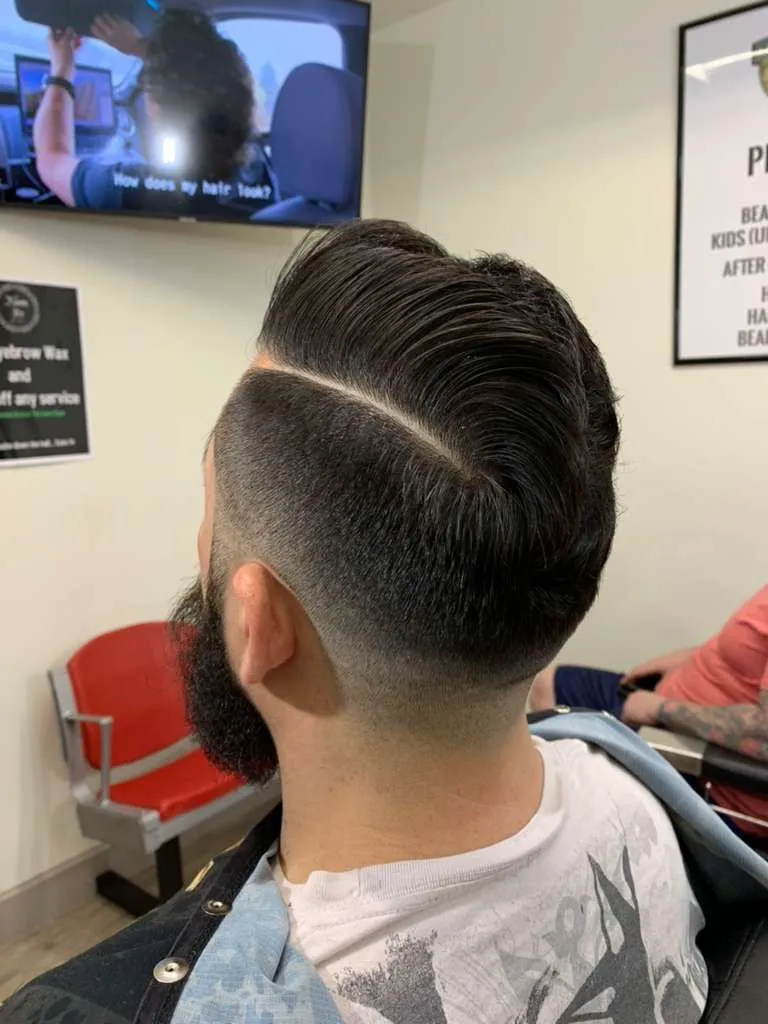 Textured quiff with a hard part and mid fade, beard shaped and lined, cut at The Cave Hype in North Phoenix